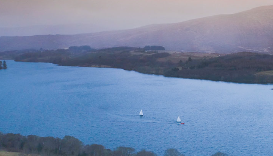 Two sailboats on a lake with forestry covering the banks and mountains in the background