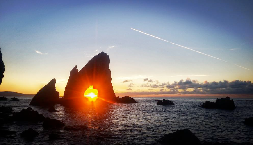 Sea arch with sun setting in the arch and a plane flying in the distance in the background