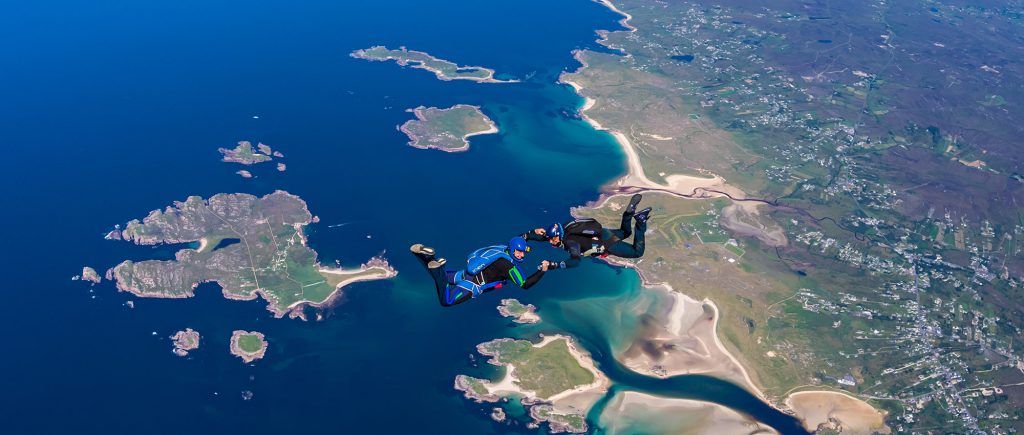 Two people, holding hands, skydiving off the coast of Donegal with several islands in the background